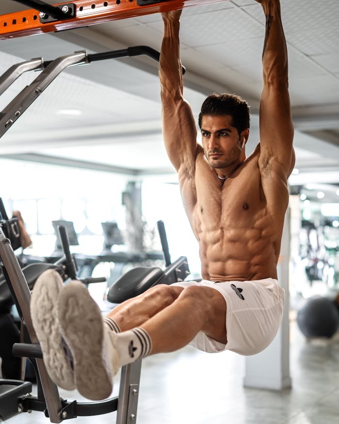 A muscular man focuses on strength training indoors, showcasing his physique during an intense gym workout.